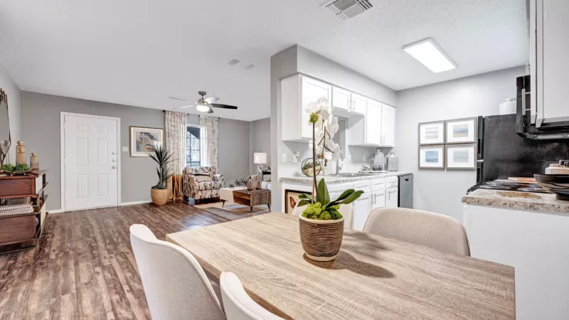  Open-concept dining and kitchen area featuring a light wood dining table with elegant chairs, modern white cabinetry, and stainless steel appliances. The space is bright and airy, with wood-style flooring and decorative touches, creating a welcoming and functional environment.