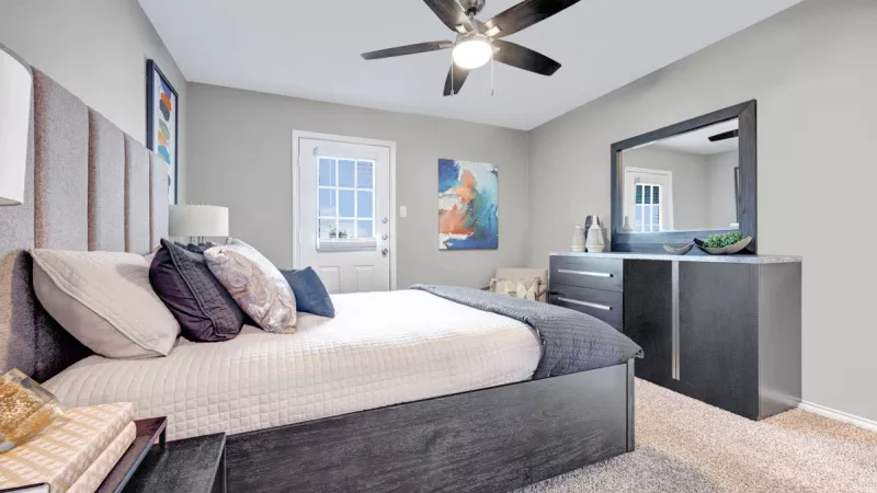 Spacious bedroom with a modern design featuring a large upholstered bed, stylish furniture, neutral tones, and a ceiling fan, creating a cozy and elegant atmosphere.
