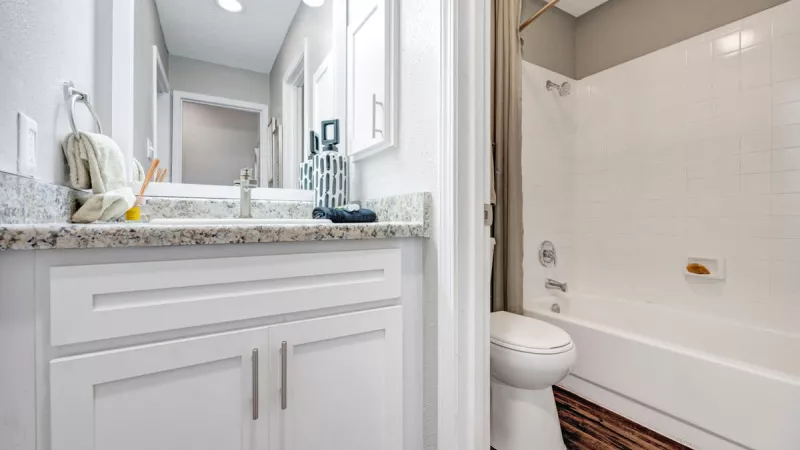  Modern bathroom featuring a sleek white vanity with ample storage, granite countertop, and a clean bathtub-shower combination, creating a fresh and functional space.