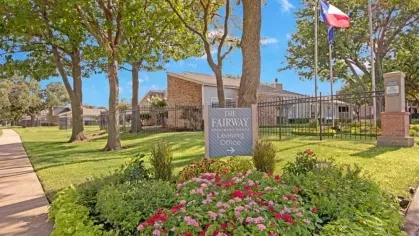A vibrant flower garden and manicured landscape featuring a sign for "The Fairway Apartments Leasing Office."
