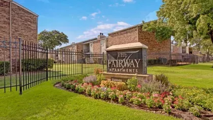A gated entrance showcasing the "The Fairway Apartments" sign surrounded by colorful flowers and greenery.