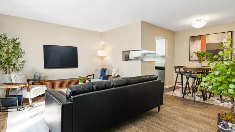 An open-concept living and dining area with a black leather sofa, a small dining table, and access to a compact kitchen.