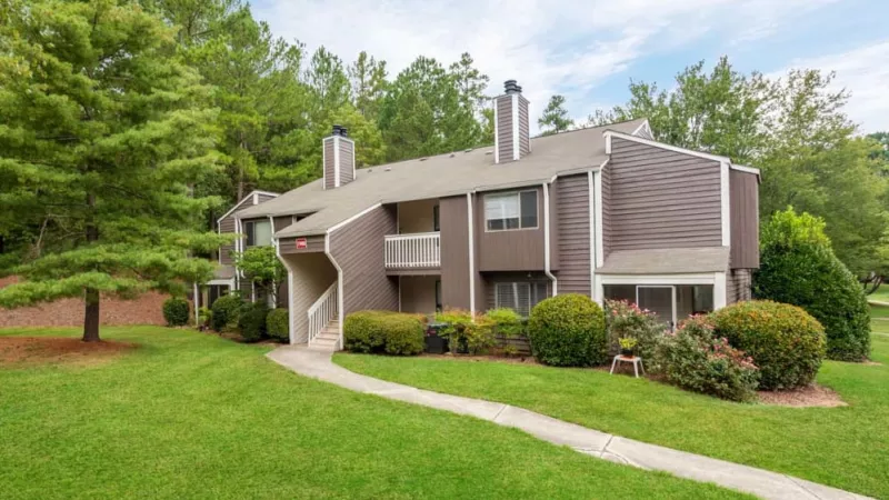 A charming apartment building with wooden siding and balconies, surrounded by manicured greenery and trees.