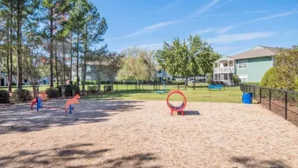 A children’s play area with colorful play equipment, trees, and a fenced grassy space for outdoor activities.