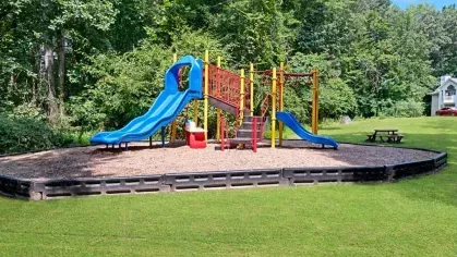 A children's playground with colorful slides and swings surrounded by greenery.