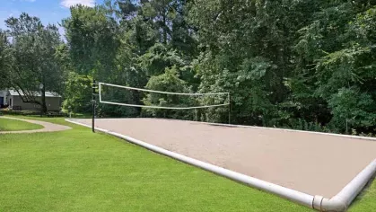 A sand volleyball court nestled among tall trees and grassy areas.