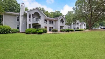 A wide lawn with trees and multiple gray apartment buildings in the background.