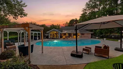 A serene pool area at sunset with lounge chairs, umbrellas, and a clubhouse in the background.