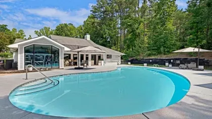 An outdoor swimming pool with forested surroundings and a clubhouse in the background.