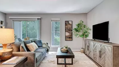 A spacious living room with a comfortable sofa, coffee table, and bright natural light coming through large windows.