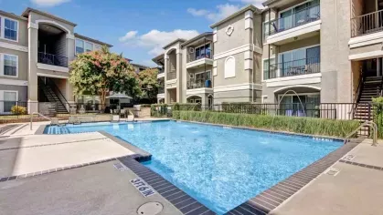 Apartment pool with a spacious deck and vibrant greenery offering a relaxing community space.