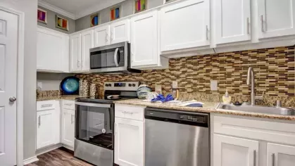 A modern kitchen with white cabinets, stainless steel appliances, granite countertops, and a tiled backsplash.