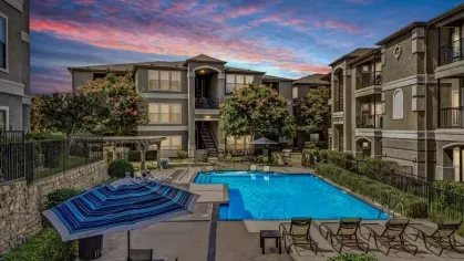 Evening view of a brightly lit pool area with surrounding residential buildings and a vibrant sunset sky.