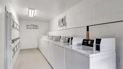 A clean and organized laundry room with rows of washers and dryers, illuminated by bright overhead lighting.