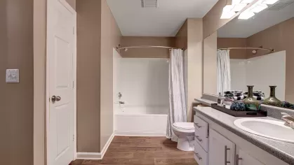 A spacious bathroom showcasing hardwood floors, a large mirror, and a bright white bathtub.