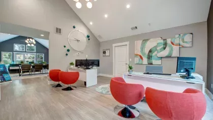 A modern leasing office with red chairs, a large clock, and vibrant wall art.