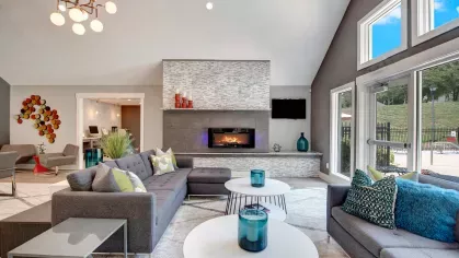 A stylish community lounge featuring cozy gray sofas, a fireplace, and large windows overlooking the pool area.