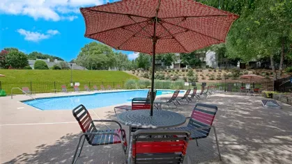 A vibrant poolside scene with a large umbrella and lounge chairs surrounding the pool area.