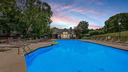 An illuminated swimming pool area at dusk, surrounded by lounge chairs and a landscaped hill at 200 Braehill Apartments.