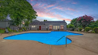 A well-lit swimming pool at sunset with a clubhouse in the background at 200 Braehill Apartments.