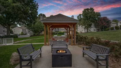 A fire pit surrounded by benches and chairs in a landscaped outdoor area at 200 Braehill Apartments.