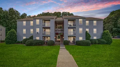 A three-story apartment building with balconies and manicured greenery at sunset at 200 Braehill Apartments.