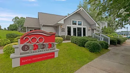 The main entrance and rental information center of 200 Braehill Apartments, featuring a red sign and well-maintained landscaping.