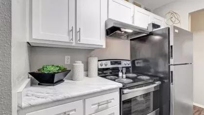 A modern kitchen featuring white cabinets, marble-style countertops, and stainless steel appliances, including a black refrigerator and oven, with stylish decor accents.