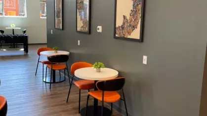 A cozy nook with small round tables and orange chairs along a gray wall adorned with artwork.
