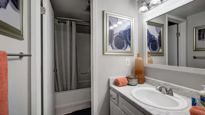 A bathroom featuring a marble countertop, framed artwork, and a shower-tub combo with a curtain.