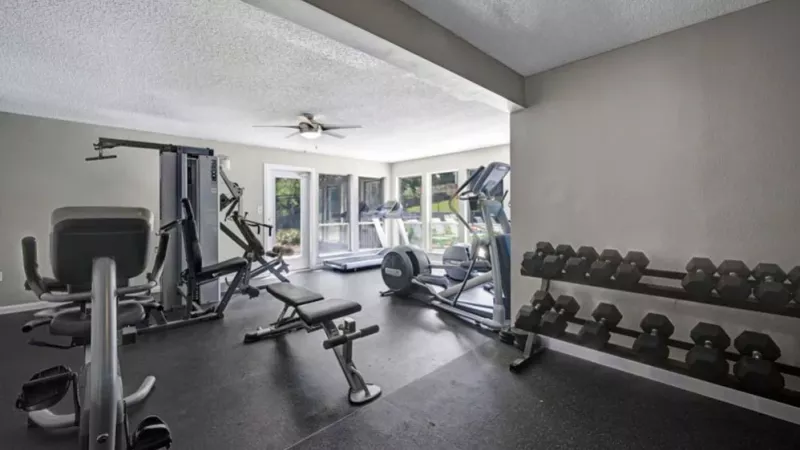 A fitness center with weightlifting and cardio equipment, featuring large windows for natural light.
