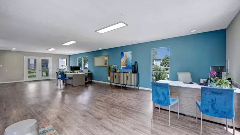 A bright community room with desks, chairs, and windows allowing natural light to fill the space.