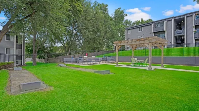 A landscaped courtyard with a pergola and outdoor seating surrounded by lush greenery and apartment buildings.