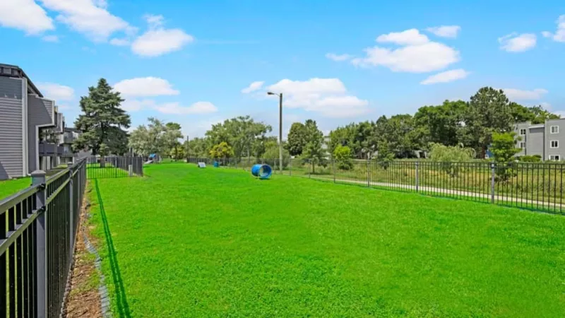 A large fenced-in green space with open grassy areas and distant views of neighboring apartment complexes.