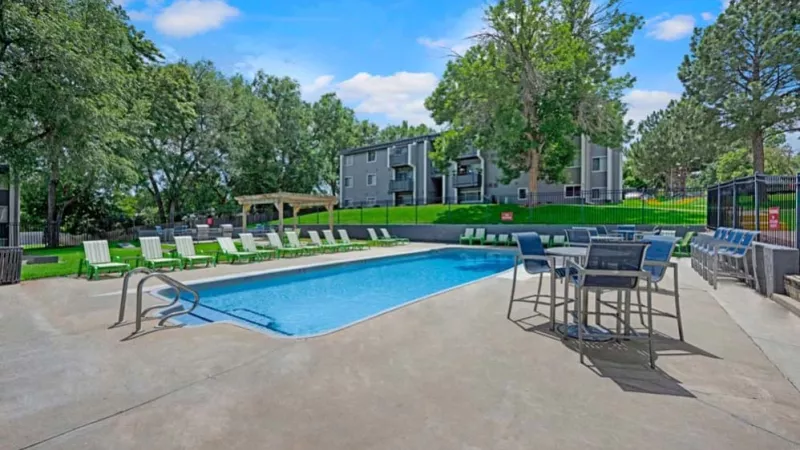 A sparkling outdoor pool surrounded by lounge chairs, patio tables, and vibrant greenery.