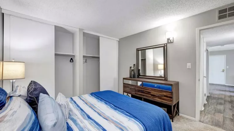 A bedroom with a blue and white striped comforter, a dresser, and sliding closet doors under soft ambient lighting.