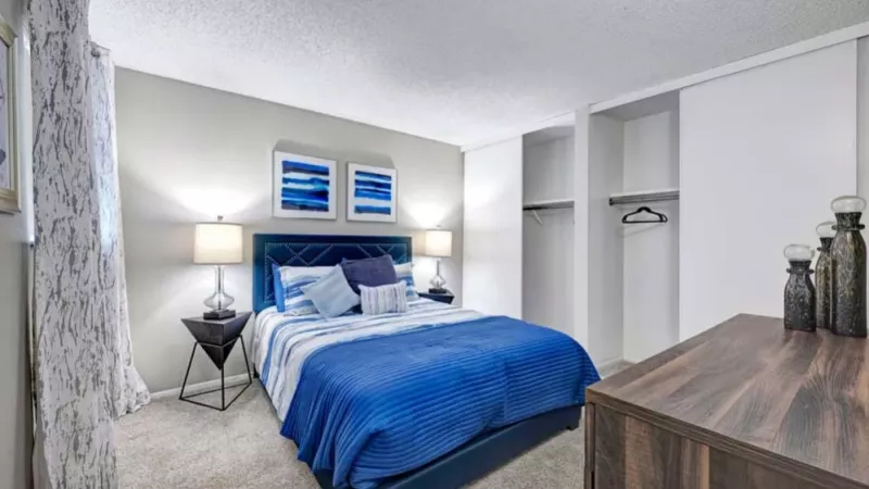 A modern bedroom with blue and white bedding, framed artwork, and ample closet space.