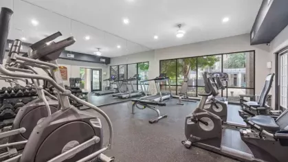 Another view of the fitness center showing exercise bikes, treadmills, and wall mirrors with ample natural light.