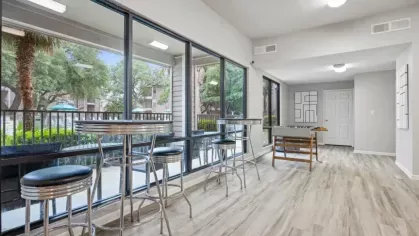 A recreational area with high-top tables and large windows providing views of the pool area and greenery outside.