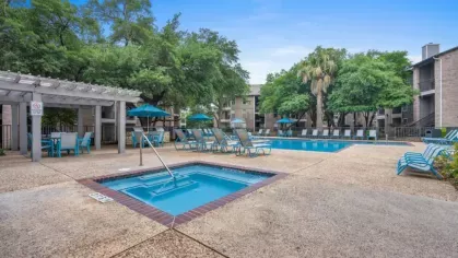 A serene pool surrounded by lush greenery and lounge chairs, illuminated under the evening sky.