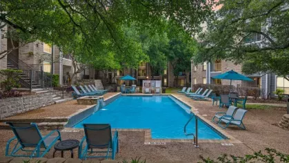 A modern clubhouse lounge with wicker seating, a kitchenette, and warm-toned decor.
