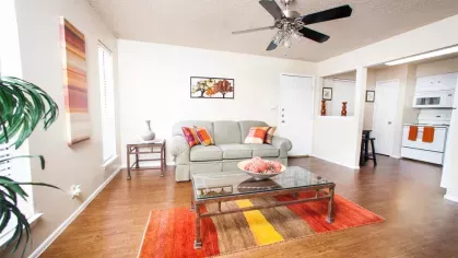 A living room with green floral cushions, a white sofa, and a modern coffee table against hardwood flooring.