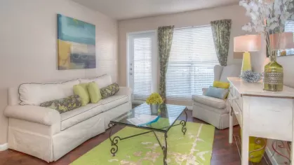 A bedroom with a colorful quilt, patterned curtains, and a wall-mounted circular mirror reflecting the soft lighting.
