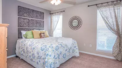 A bright and cheerful living room with soft furnishings, modern artwork, and ample natural light filtering through wide windows.
