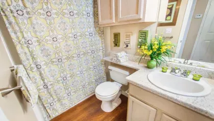 A brightly decorated bathroom featuring patterned curtains, a countertop with a vase of yellow flowers, and a clean white sink.