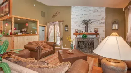 A spacious clubhouse with multiple leather sofas, a vibrant orange accent wall, and large windows with natural light.