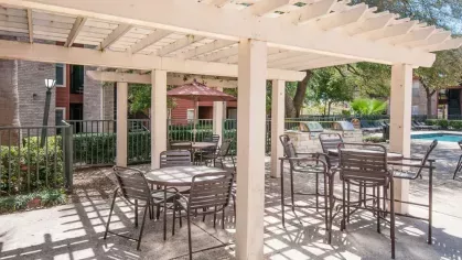 Another shaded pergola with metal chairs and tables, surrounded by lush greenery and near a swimming pool.