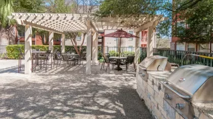 A barbecue grill area featuring pergolas and outdoor dining spaces within a landscaped apartment complex.