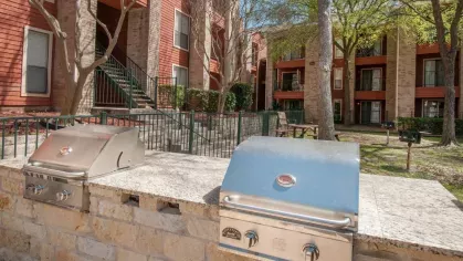 Stainless steel outdoor grills against a stone countertop in a courtyard of an apartment community.