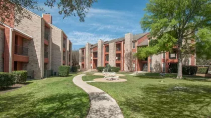 A courtyard view with winding walkways, picnic tables, and lush green lawns nestled between apartment buildings.
